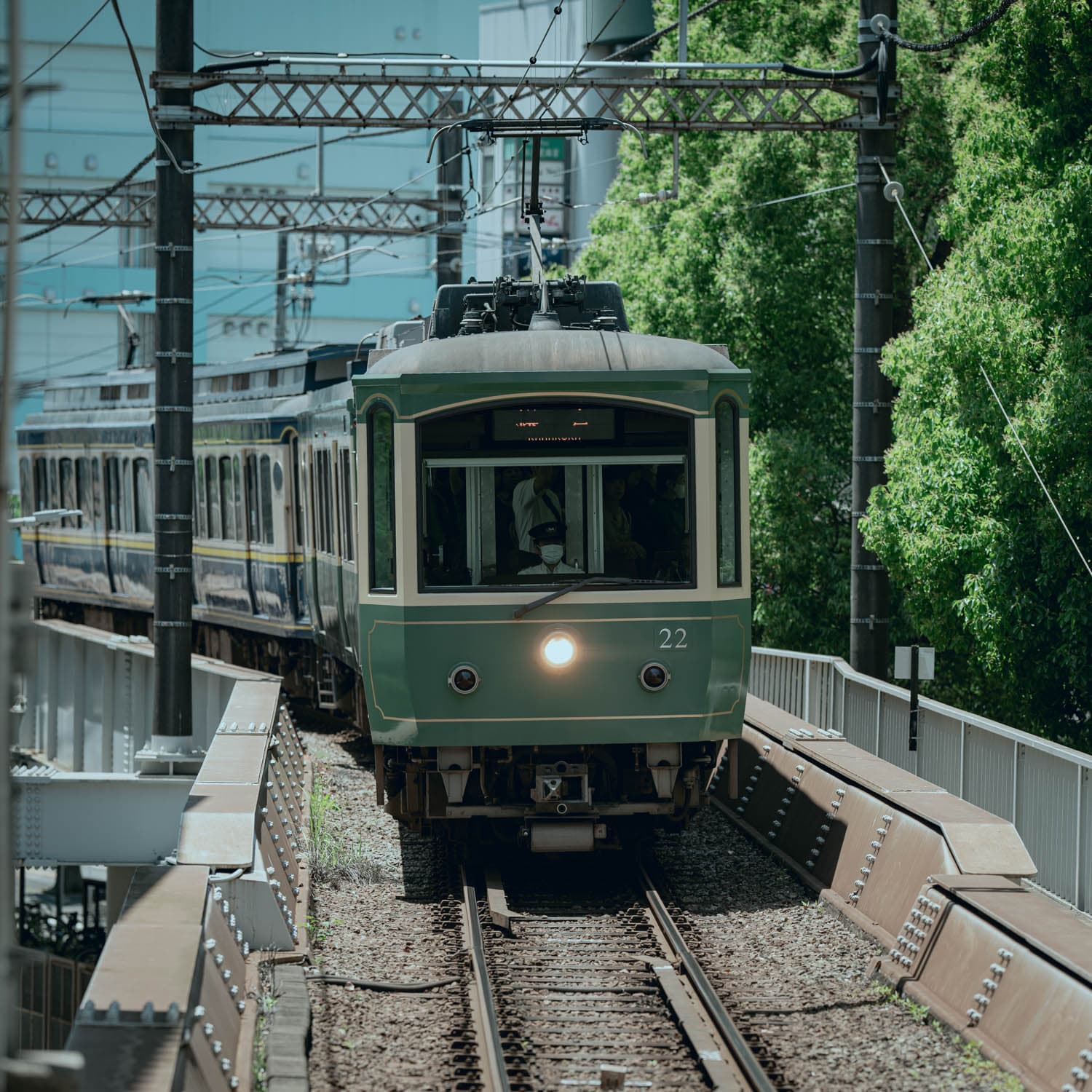 A green train traveling on railway tracks surrounded by greenery and overhead power lines