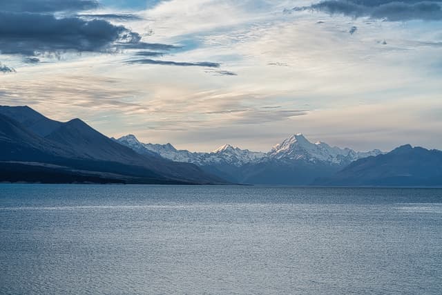 A serene lake with a backdrop of snow-capped mountains under a partly cloudy sky