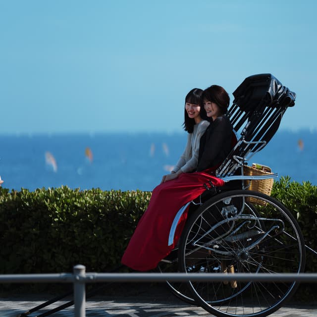 Two women sitting in a rickshaw by the seaside, with a clear blue sky and ocean in the background