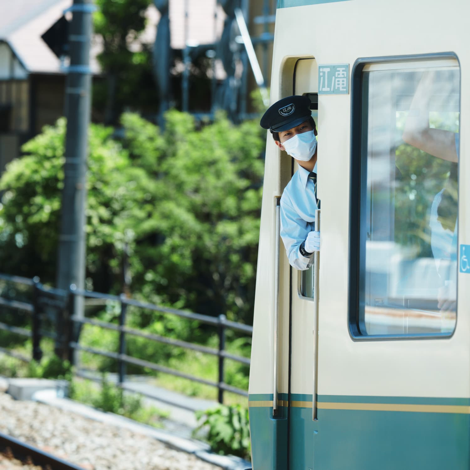 A train conductor wearing a mask and uniform looks out from the door of a train