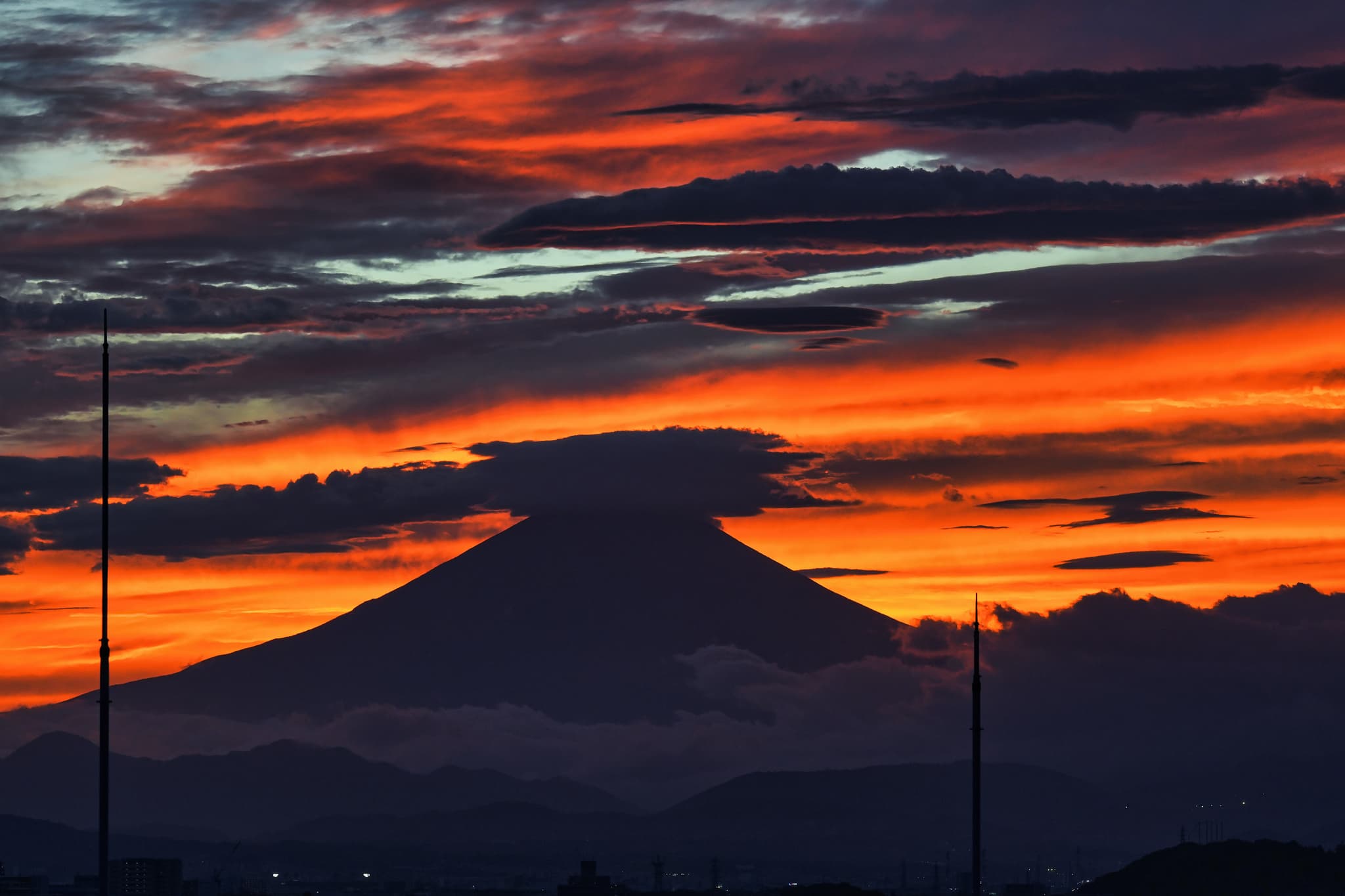 A silhouetted mountain against a dramatic sunset sky with vibrant orange, red, and purple hues, and scattered clouds